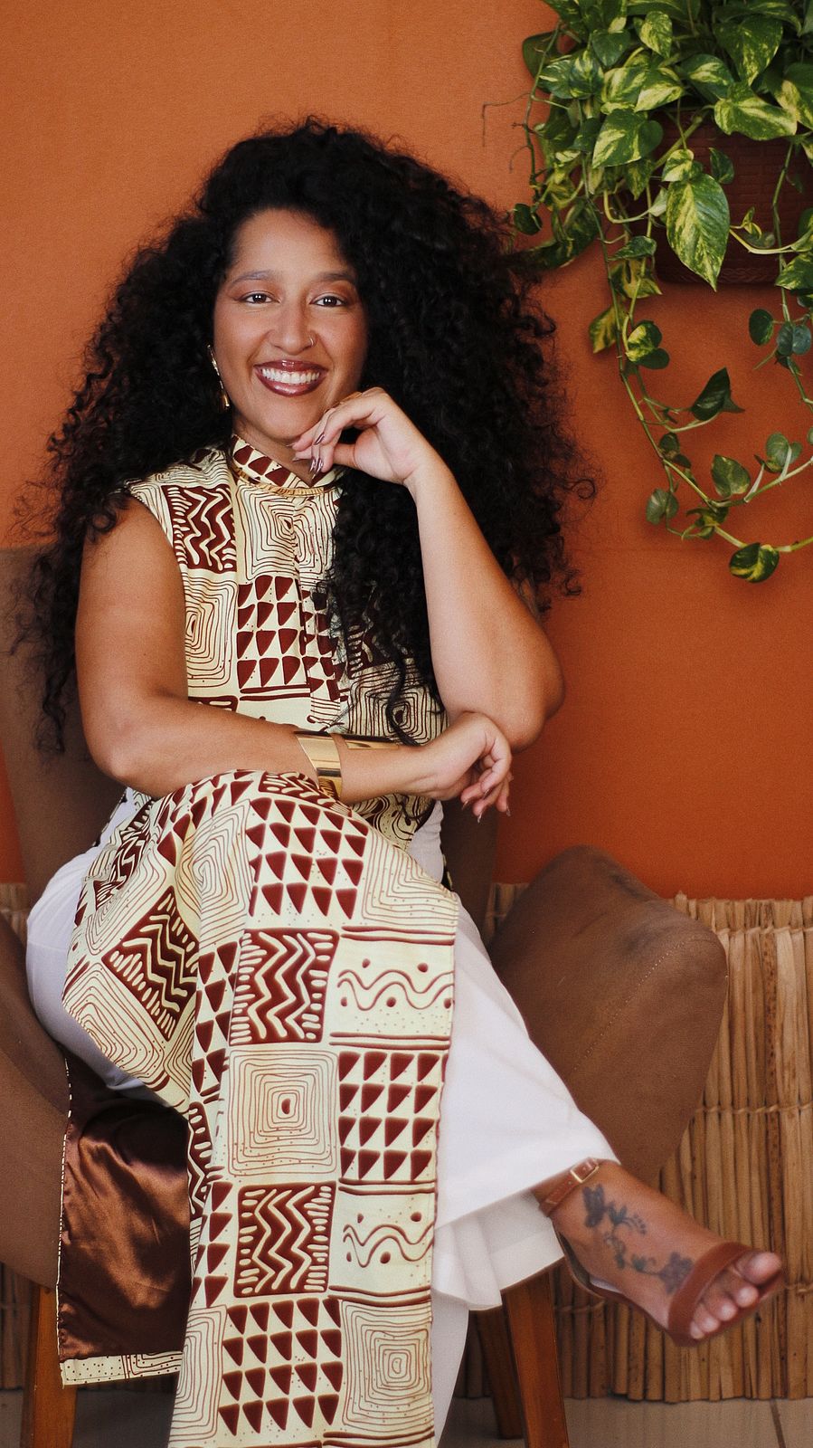 Marina Niambi sorrindo, sentada de pernas cruzadas em ambiente acolhedor